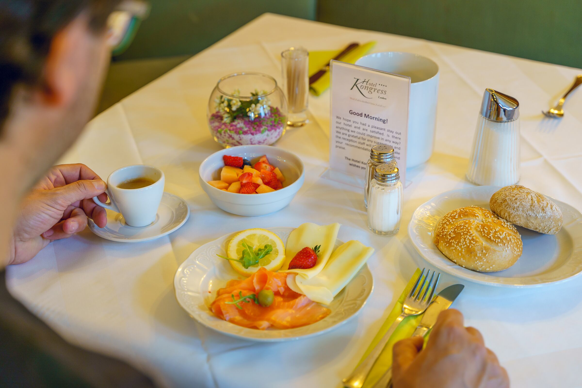 Breakfast table with a plate of salmon and cheese, buns, a fruit salad and a cup of coffee