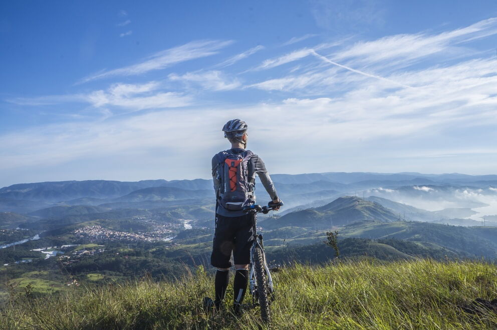 Mountainbiker mit seinem Rad auf einem Berg mit Aussicht auf die atemberaubende umliegende Bergwelt; © Fabricio Macedo FGMsp auf Pixabay
