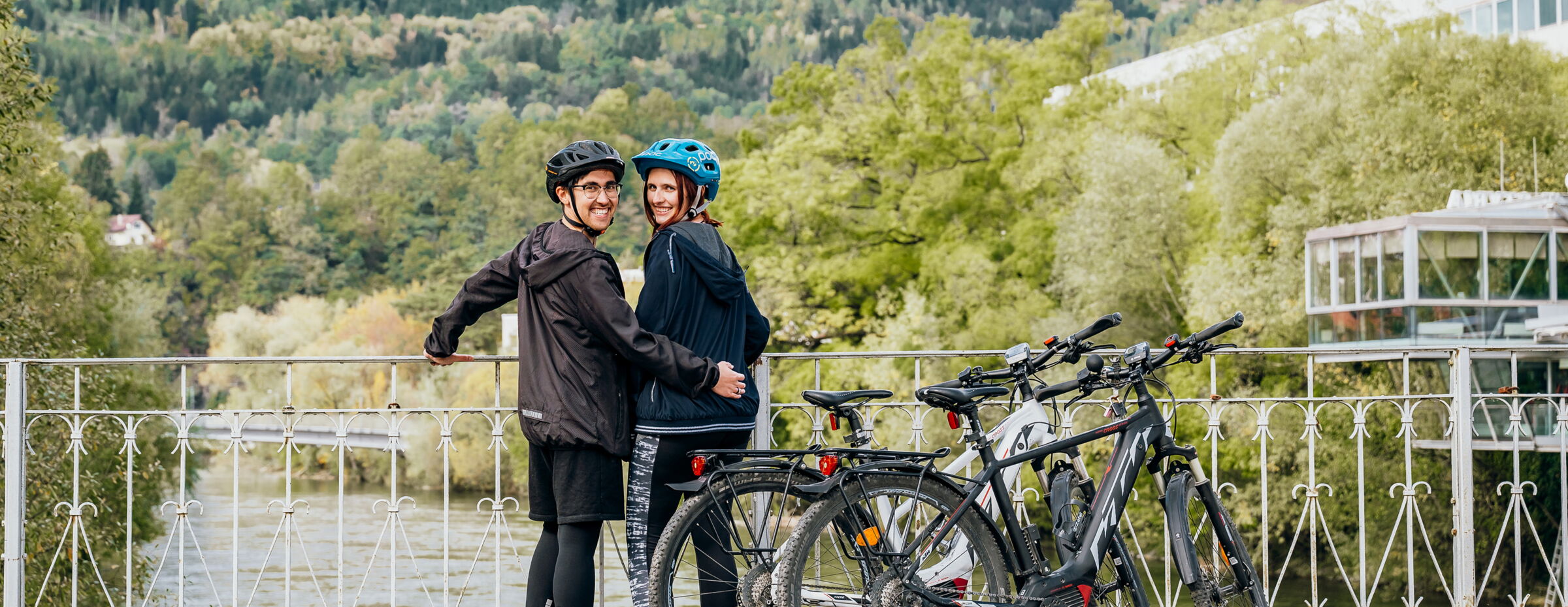 Two cyclists stand on a bridge with a view of the landscape; © www.erzberg-leoben.at